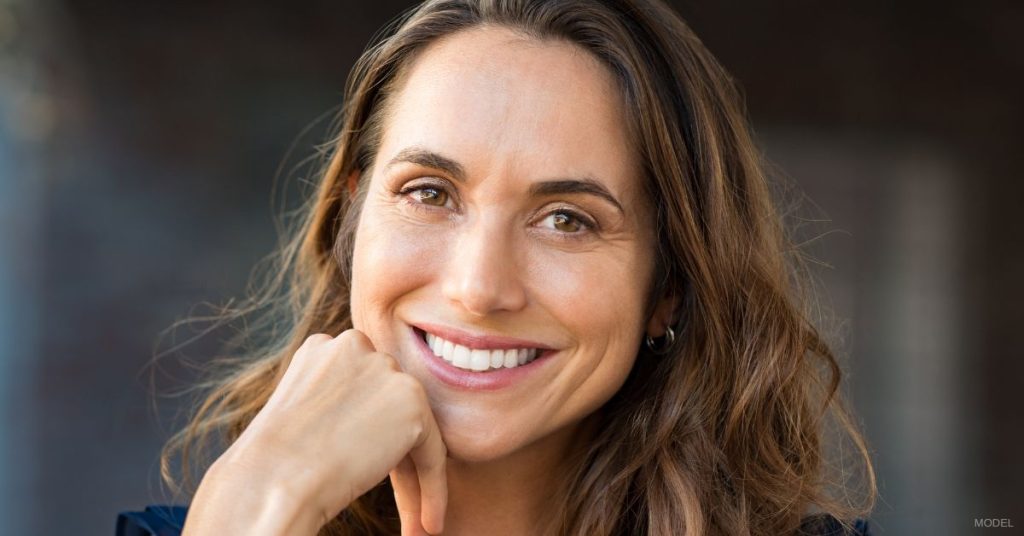 A woman smiling with their hand on their chin. (Model)