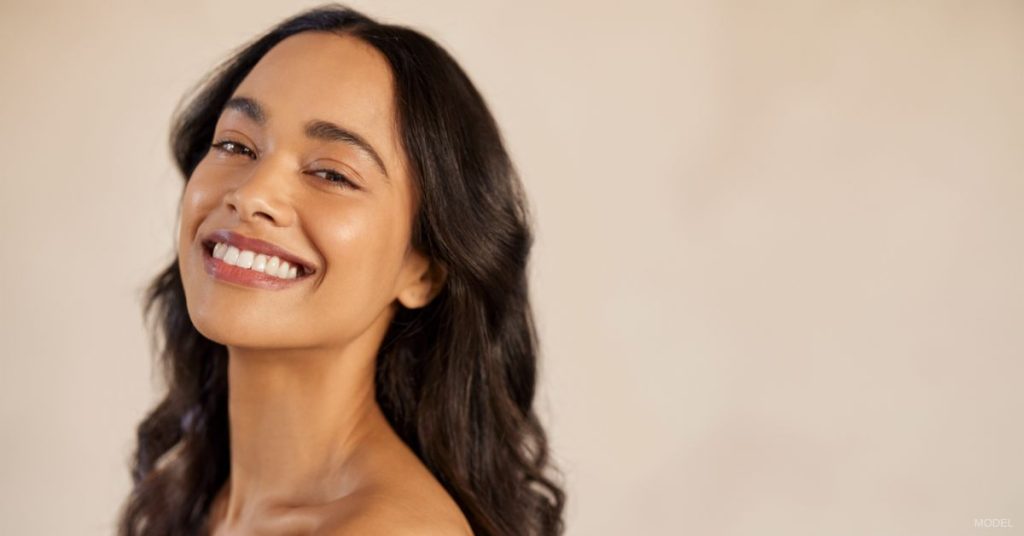 A woman with long dark hair is smiling. (Model)